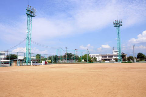 左側と右奥に水色のナイター用の投光器が2台設置され、その間に同じ水色のバックネットがある、土で整備された中山町民グラウンドの写真