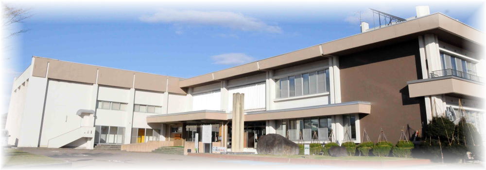 白と茶色の外壁で、屋根やバルコニー部分がベージュのL字型2階建ての中央公民館の外観写真