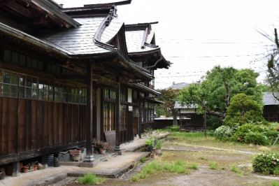 右側に所々花を咲かせた草木の庭、左側に木造の雨戸を閉めた柏倉惣右衛門家住宅の外観写真