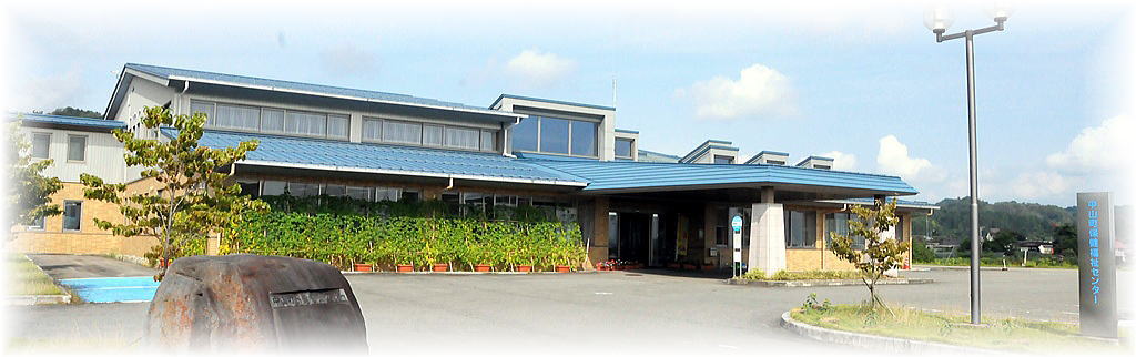 2階建て横長の三角屋根で、エントランスには雨除け付きの降車スペースとバス停が設けられた中山町保健福祉センターの外観写真