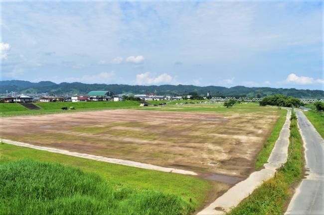 山々を背景に街並みや右奥に長崎大橋が見える広大な面積がある運動広場の写真